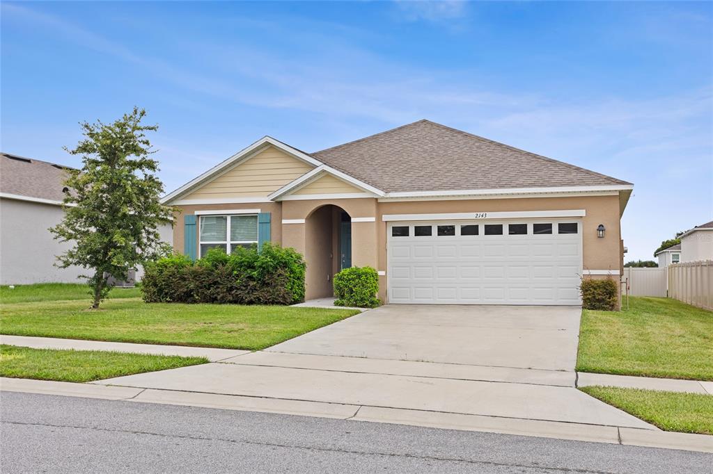 A single-story suburban house with a tan stucco exterior, beige siding, and a two-car garage — 2143 KALIN WAY, TAVARES, FL