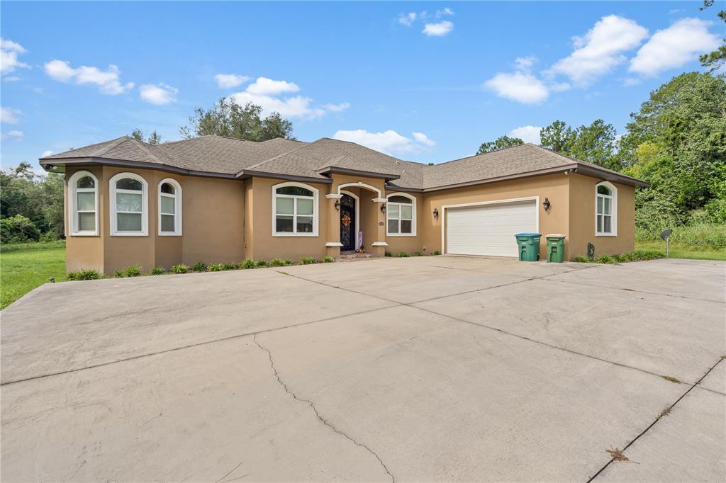 A single-story tan stucco house with a concrete driveway and an attached two-car garage — 16635 SW 139TH AVENUE, ARCHER, FL