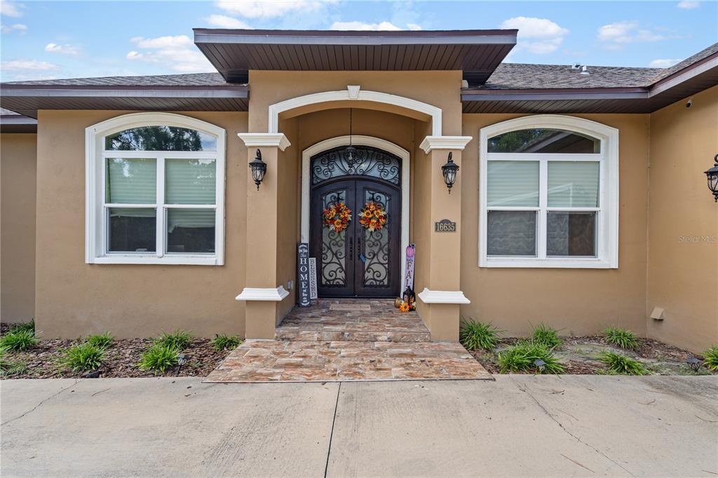 The exterior of a tan house features a stone-tiled entryway and double arched front doors — 16635 SW 139TH AVENUE, ARCHER, FL