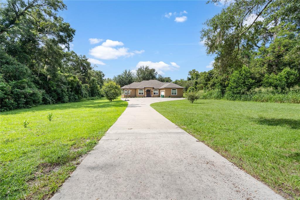 A long concrete driveway leads to a single-story house surrounded by trees and grass — 16635 SW 139TH AVENUE, ARCHER, FL