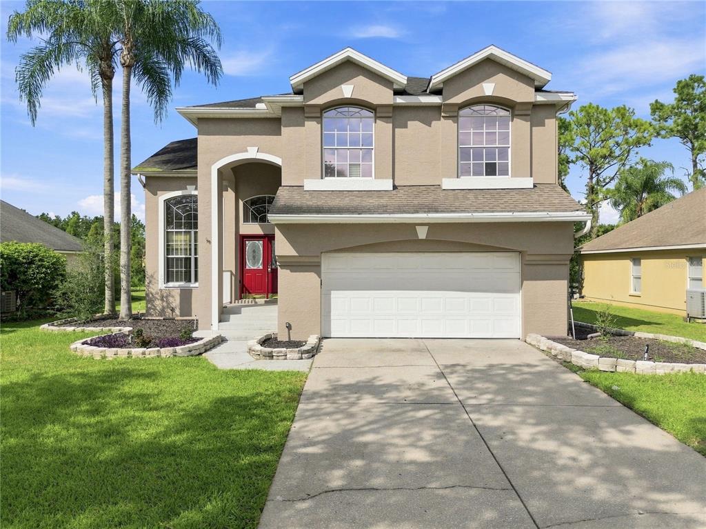 A two-story suburban house with a tan stucco exterior, a red front door, and a garage — 7326 YARDLEY WAY, TAMPA, FL