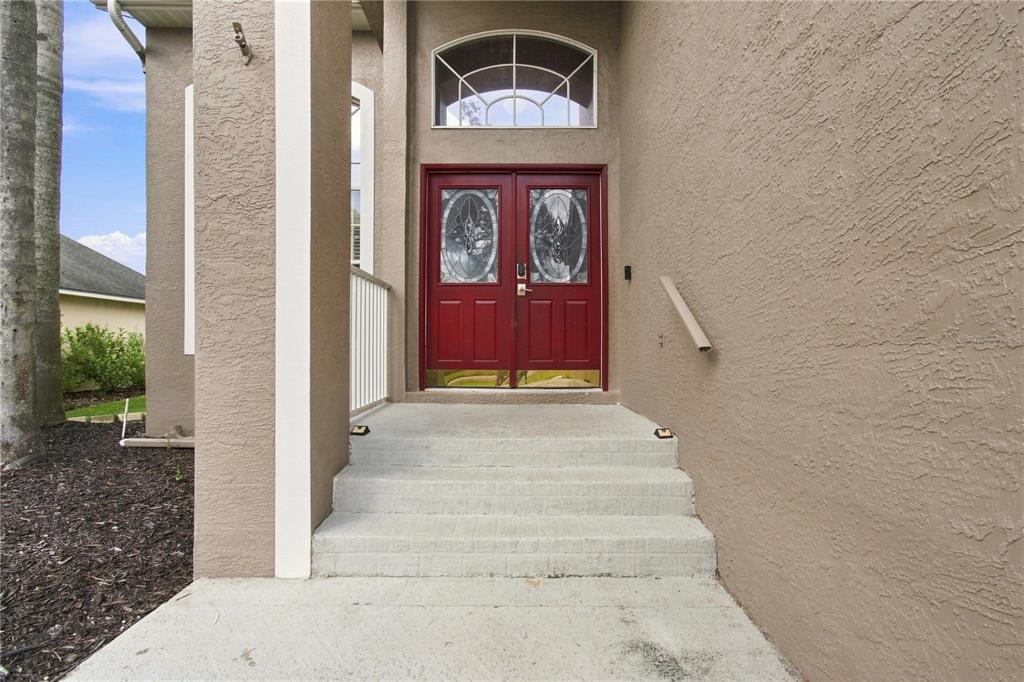 A red double front door with glass inserts sits at the top of concrete steps — 7326 YARDLEY WAY, TAMPA, FL