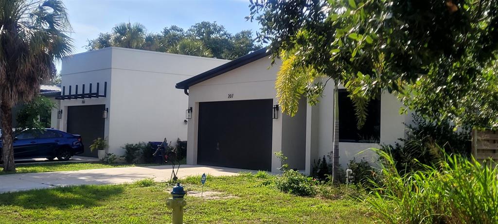 Two modern, white single-story houses with dark garage doors sit side-by-side on a grassy lot — OLD TRAIL DRIVE, NOKOMIS, FL