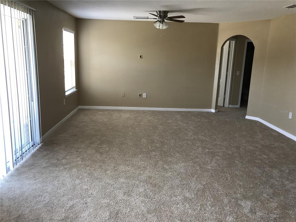 An empty living room features beige walls, tan carpeting, a ceiling fan, and sliding glass doors — 4020 PEMBERLY PINES CIRCLE, ST CLOUD, FL