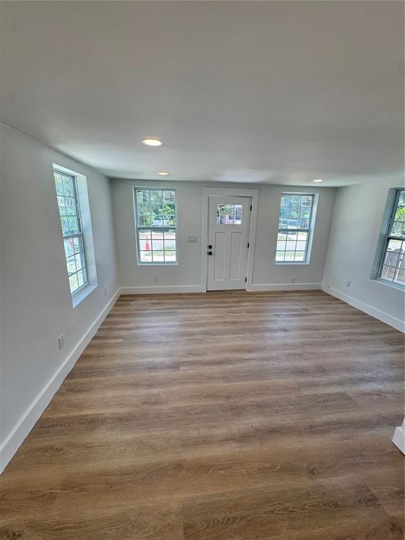 A bright, empty room with light wood-look flooring, white walls, and a central front door — 309 E WOODWARD AVENUE, EUSTIS, FL
