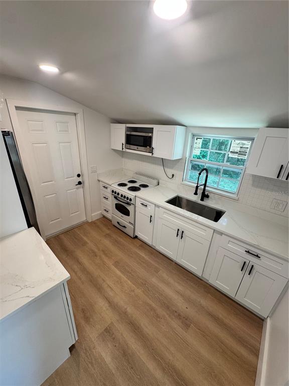 A kitchen features white cabinets, quartz countertops, a stainless steel sink, and light wood flooring — 309 E WOODWARD AVENUE, EUSTIS, FL