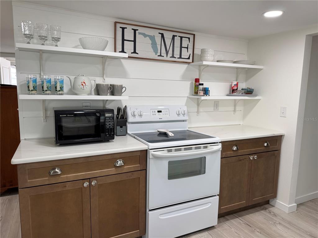 A kitchen features brown cabinets, white countertops, open shelving, and a white electric range — 1357 LAKESHORE DRIVE, MOUNT DORA, FL