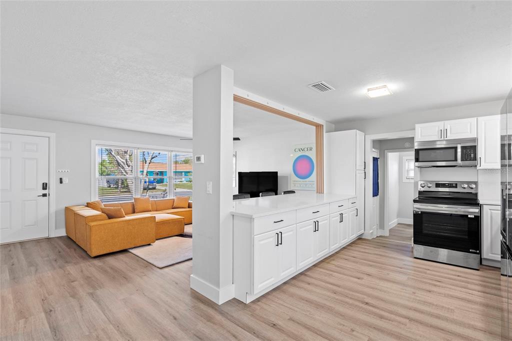 A bright kitchen with white cabinets and a peninsula overlooks a living room with seating — 2003 6TH PLACE SW, LARGO, FL