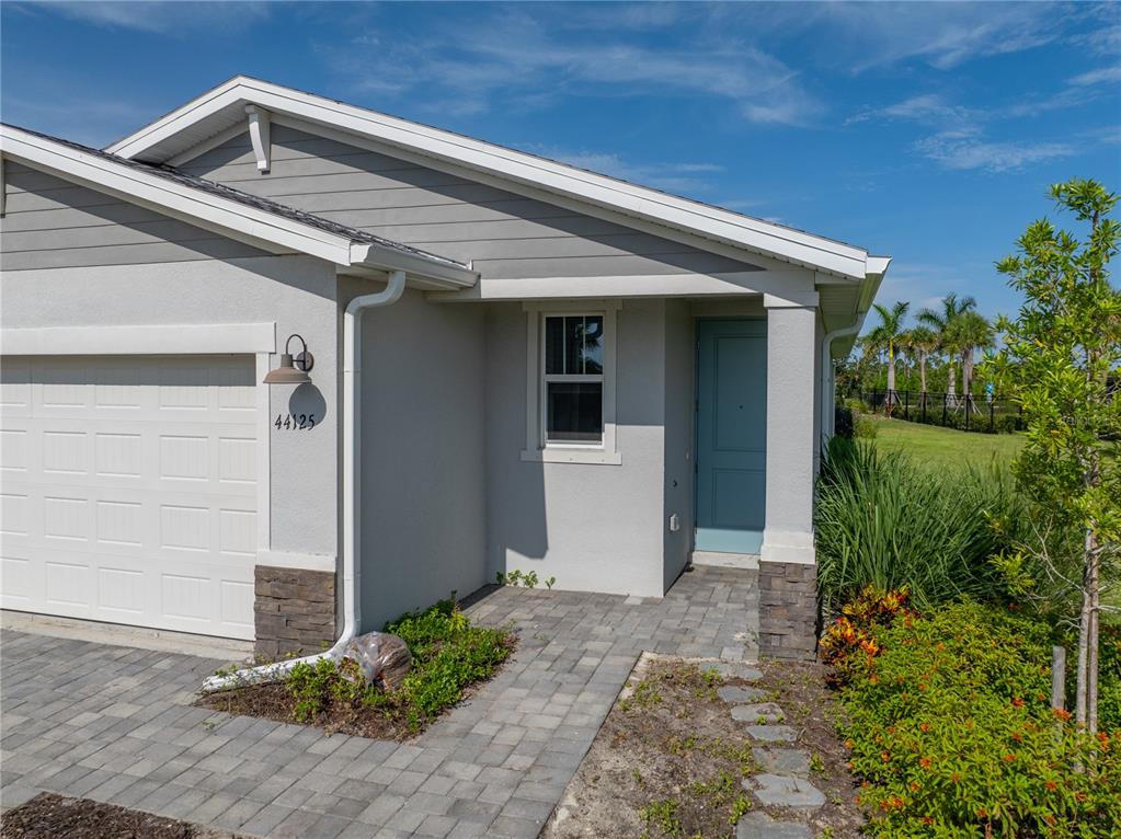 A light gray house exterior features a white garage door, a blue front door, and pavers — 44125 FRONTIER DRIVE, PUNTA GORDA, FL