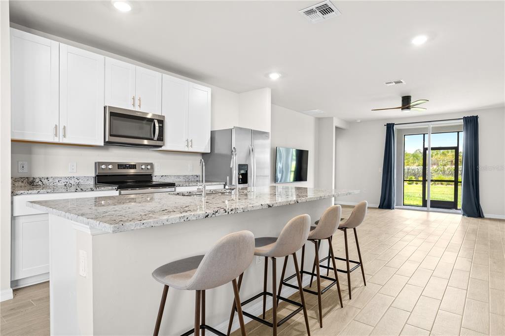 A kitchen with white cabinets, granite countertops, and an island with three bar stools — 44125 FRONTIER DRIVE, PUNTA GORDA, FL