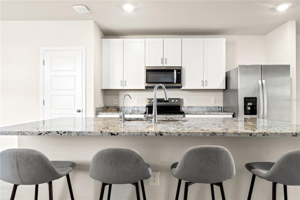 A kitchen features a granite-topped island, white cabinets, stainless steel appliances, and four gray stools — 44125 FRONTIER DRIVE, PUNTA GORDA, FL