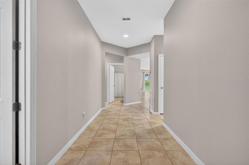 A hallway with light beige walls and tan tile flooring leads toward an open living area — 30115 CHEVAL STREET, MOUNT DORA, FL