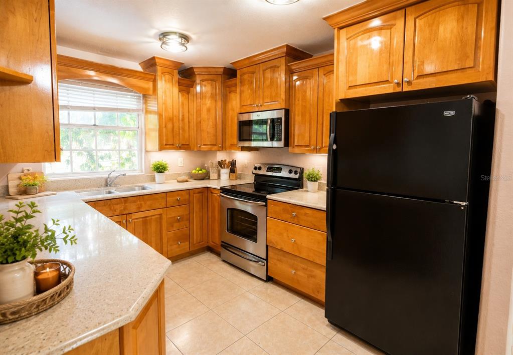 A kitchen features light wood cabinets, granite countertops, stainless steel appliances, and a black refrigerator — 2305 HAYWOOD COURT UNIT 203, MAITLAND, FL
