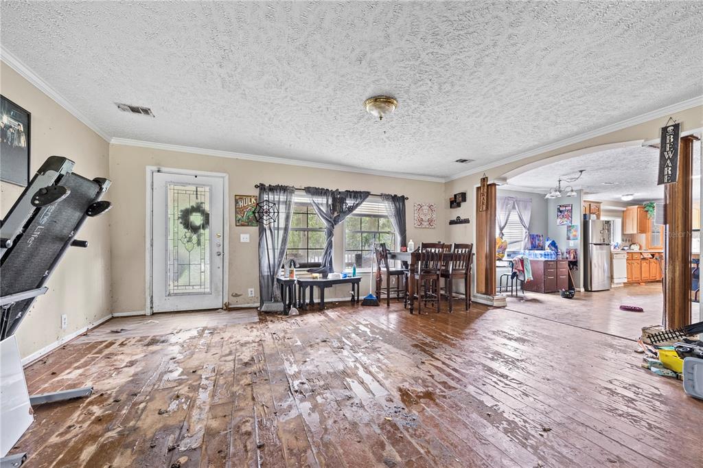 A living room with a damaged wood floor, a treadmill, and an adjacent kitchen area — 13573 98TH STREET, LIVE OAK, FL