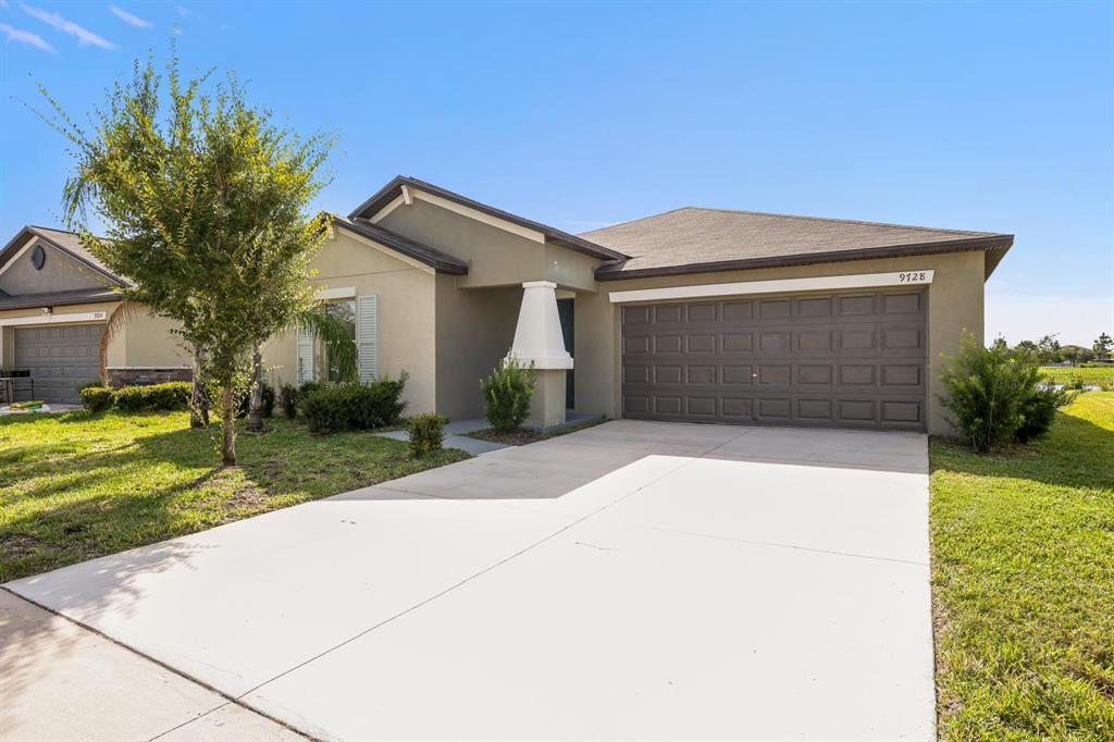 A single-story suburban house with a tan stucco exterior, a two-car garage, and a driveway — 9728 CHANNING HILL DRIVE, RUSKIN, FL