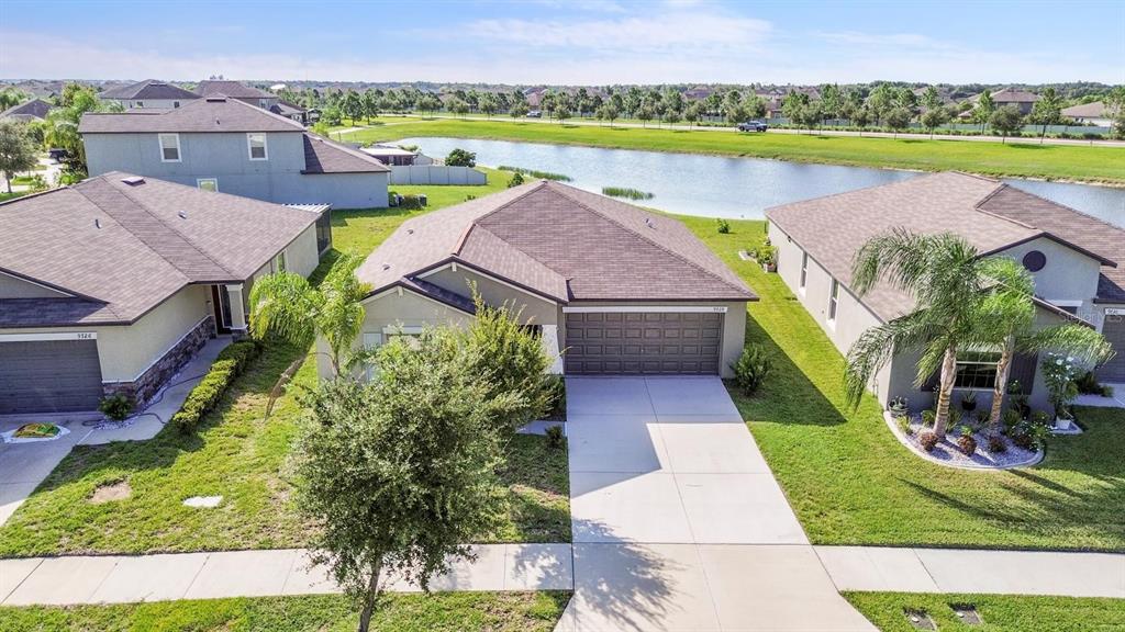 An aerial view shows three suburban houses with brown roofs and driveways near a pond — 9728 CHANNING HILL DRIVE, RUSKIN, FL