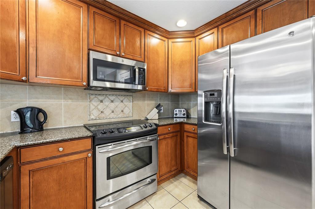 A kitchen with wood cabinets and granite countertops opens to a living and dining area — 7613 CABANA COURT UNIT 304, KISSIMMEE, FL