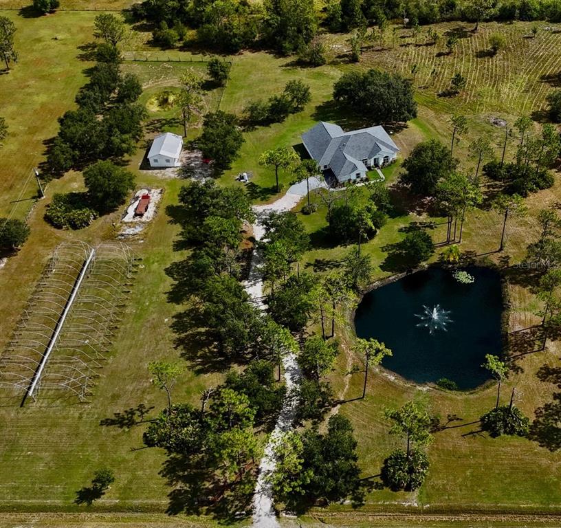 A gravel driveway leads past wooden fences and trees toward a small house and pond — 7425 245TH STREET E, MYAKKA CITY, FL
