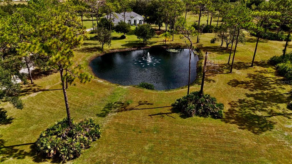 An aerial view shows a house, a detached garage, a pond with a fountain, and a greenhouse — 7425 245TH STREET E, MYAKKA CITY, FL