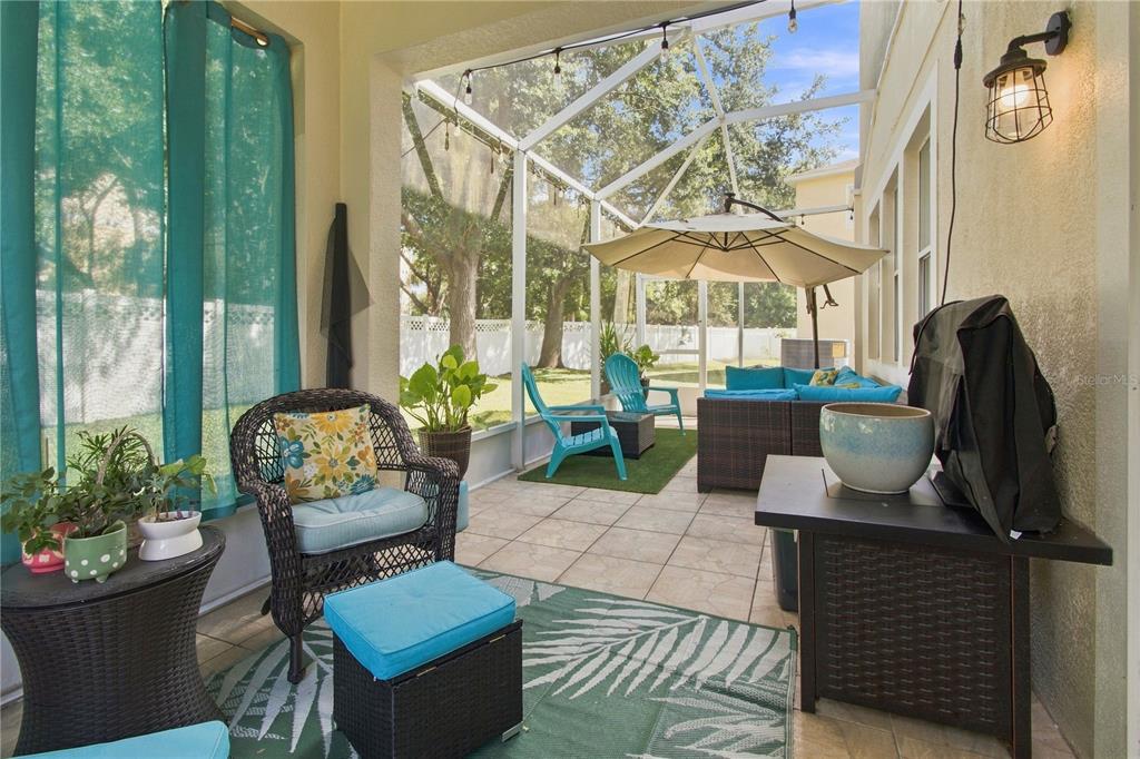 A screened-in patio features tile flooring, outdoor furniture, a patio umbrella, and a backyard view — 2340 SPRING HOLLOW LOOP, WESLEY CHAPEL, FL