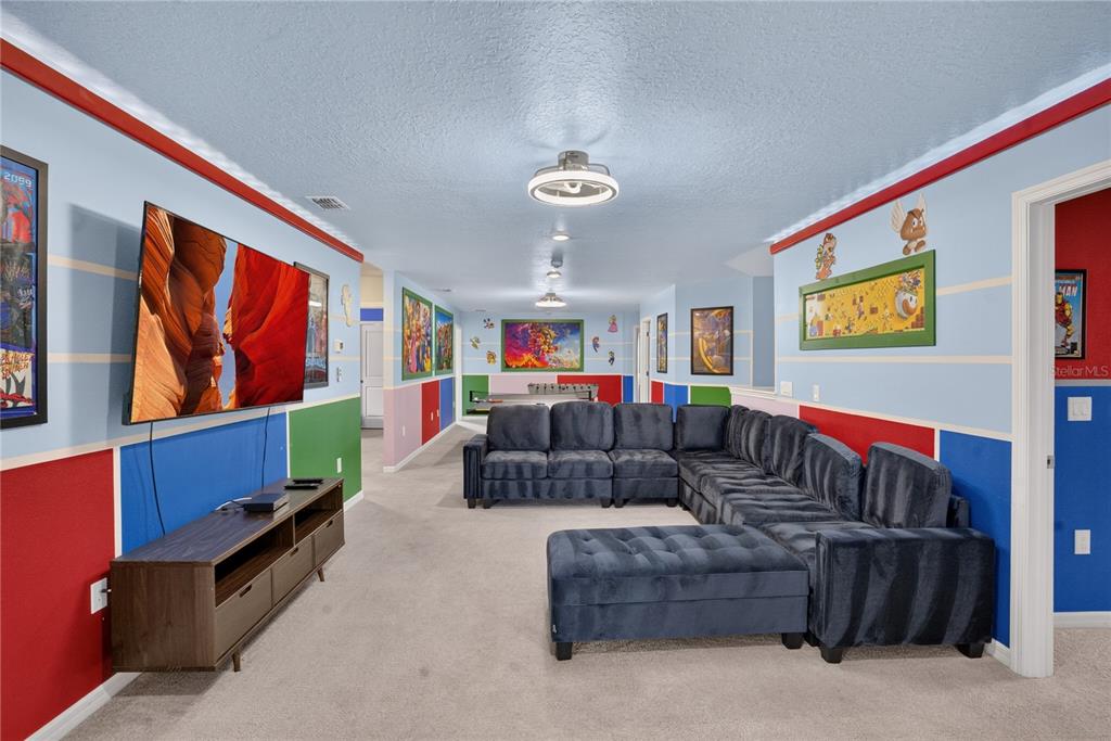 A colorful game room features a large sectional sofa, a wall-mounted television, and themed decor — 2127 LELANI CIRCLE, DAVENPORT, FL