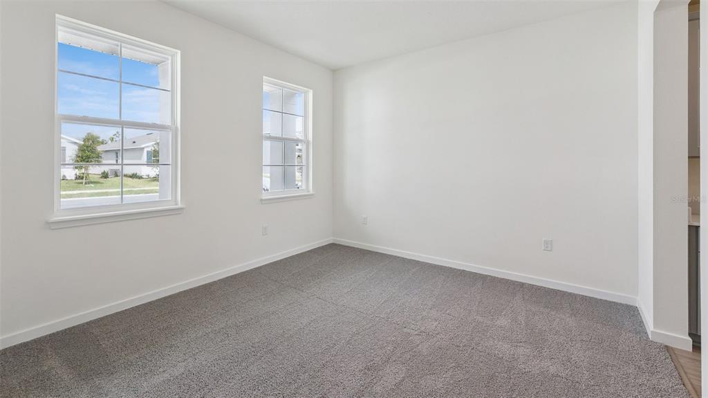 An empty room with white walls, gray carpeting, and two windows overlooking a suburban street — 3038 KINGSMAN TRAIL, ORMOND BEACH, FL