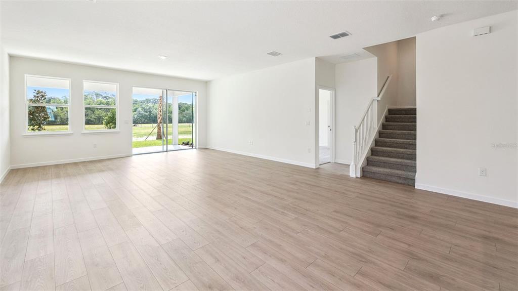 An open-concept living area features light wood-look flooring, white walls, and a carpeted staircase — 3038 KINGSMAN TRAIL, ORMOND BEACH, FL