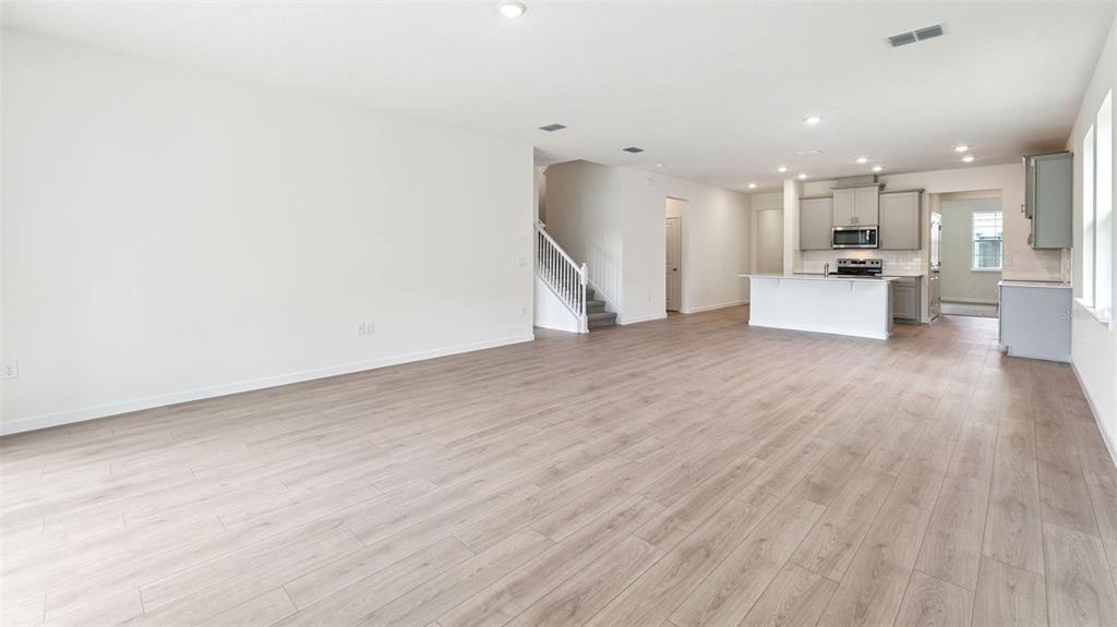 An open-concept living area features light wood-look flooring, white walls, and a kitchen with gray cabinets — 3038 KINGSMAN TRAIL, ORMOND BEACH, FL