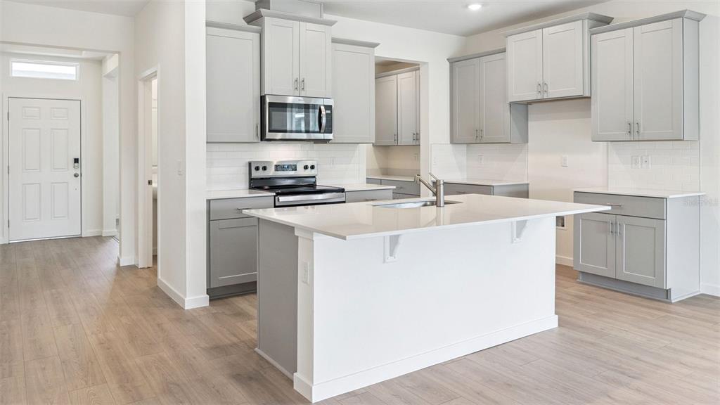 A modern kitchen features light gray cabinets, white countertops, a central island, and wood-look flooring — 3038 KINGSMAN TRAIL, ORMOND BEACH, FL