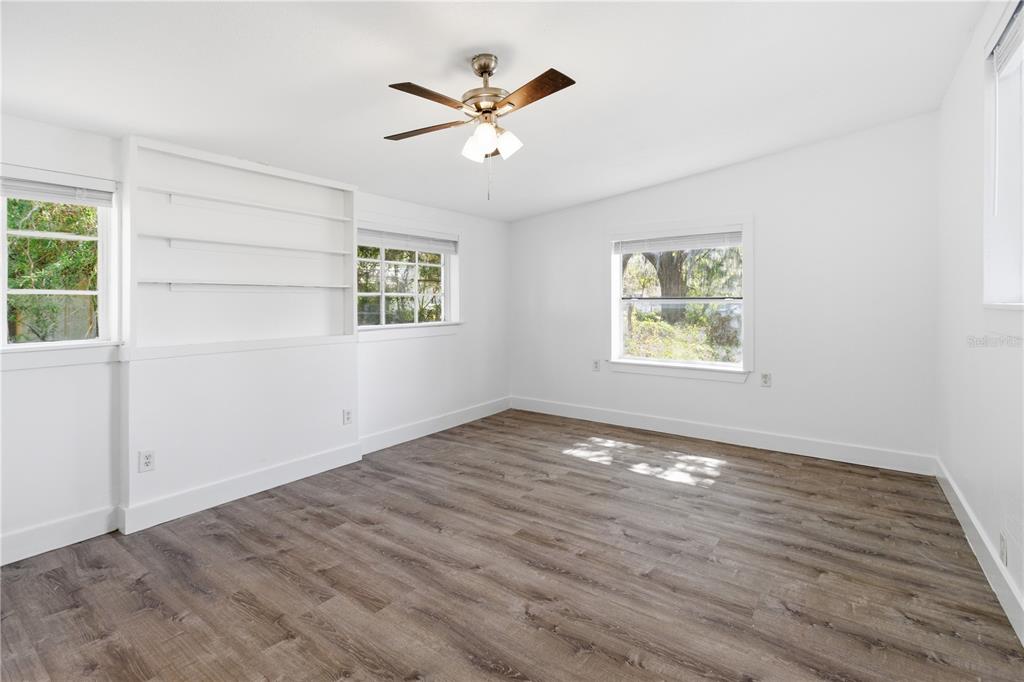 A bright bedroom features white walls, wood-look flooring, built-in shelving, and a ceiling fan — 5405 WINDERMERE DRIVE, JACKSONVILLE, FL