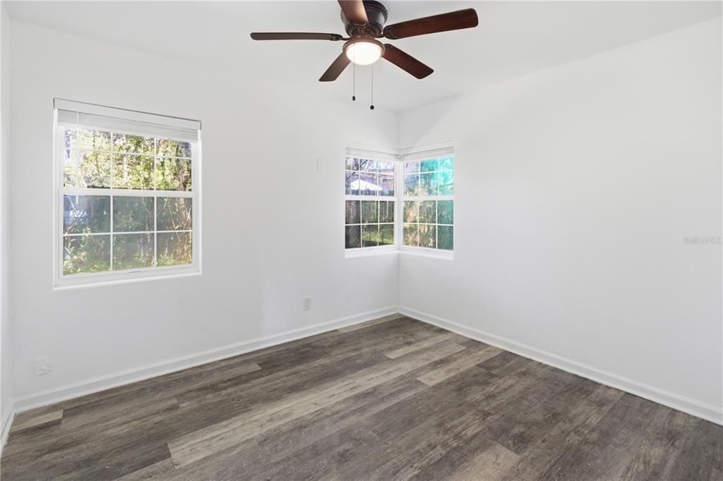 An empty bedroom features white walls, wood-look flooring, a ceiling fan, and three windows — 5405 WINDERMERE DRIVE, JACKSONVILLE, FL