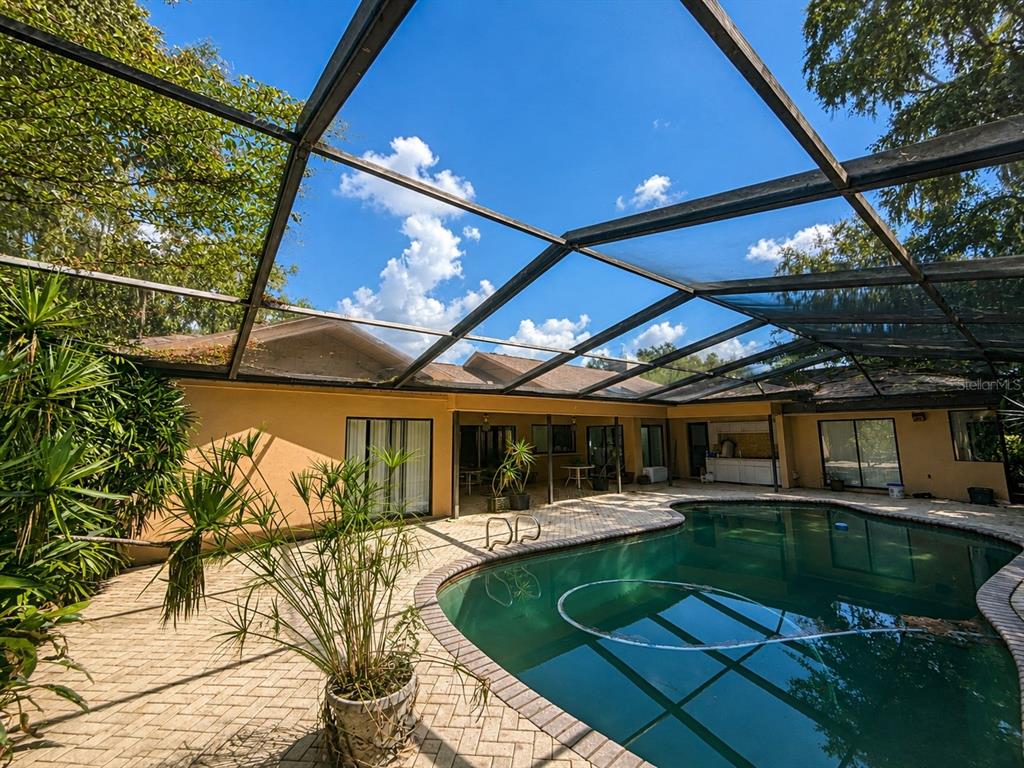 A swimming pool with a screen enclosure sits on a brick patio behind a house — 6701 PEMBERTON VIEW DRIVE, SEFFNER, FL