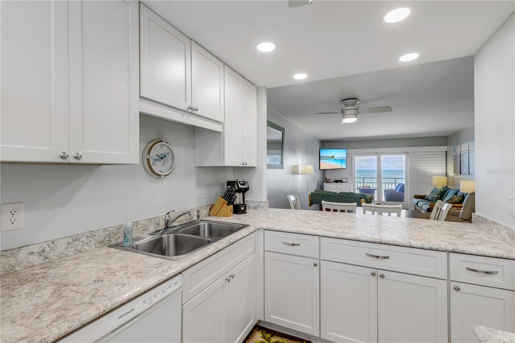 A white kitchen with stone countertops overlooks a living area with a view of the ocean — 4151 S ATLANTIC AVENUE UNIT 3030, NEW SMYRNA BEACH, FL