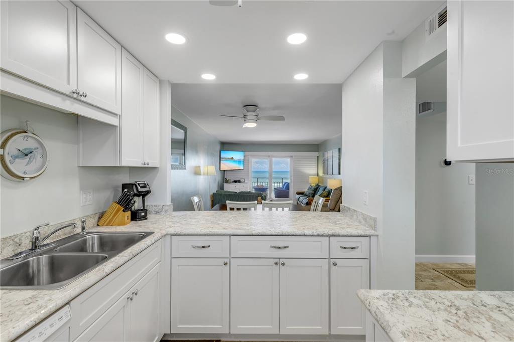 A white kitchen with stone countertops overlooks a living area with a view of the ocean — 4151 S ATLANTIC AVENUE UNIT 3030, NEW SMYRNA BEACH, FL