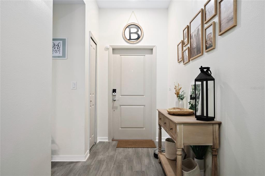 An entryway features a light-colored door, wood-look flooring, a console table, and wall-mounted picture frames — 2518 HOPTREE LANE, EDGEWATER, FL