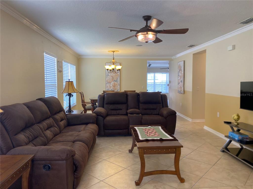 A living room with brown reclining sofas, a coffee table, and a dining area beyond — 662 ROSSELLI BOULEVARD, DAVENPORT, FL