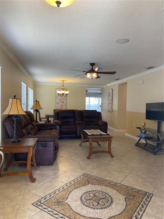 A living room features tile floors, a brown reclining sofa, a ceiling fan, and a television — 662 ROSSELLI BOULEVARD, DAVENPORT, FL