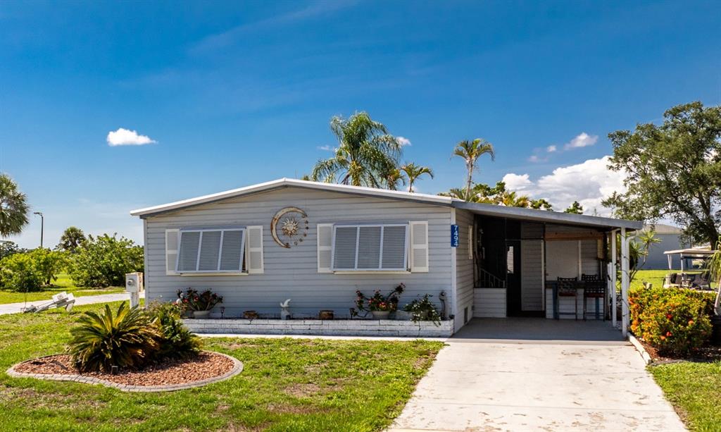 A light gray mobile home with a carport, a front garden, and a sun decoration — 7494 DANVERS CIRCLE, PORT CHARLOTTE, FL