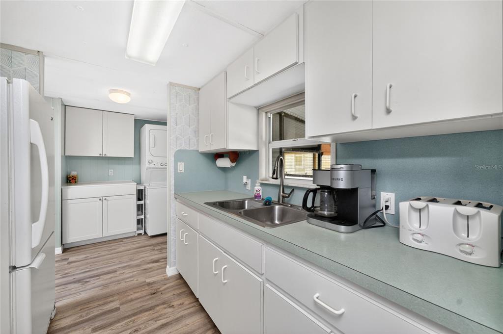 A kitchen features white cabinets, light blue walls, a double sink, and wood-look flooring — 7494 DANVERS CIRCLE, PORT CHARLOTTE, FL