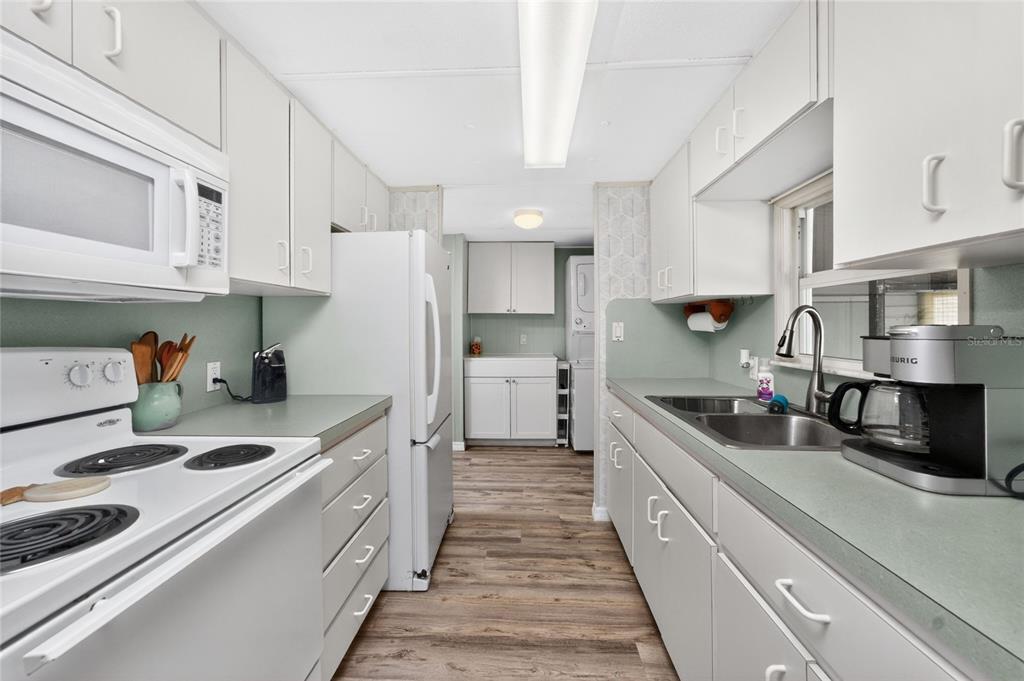 A galley kitchen features white cabinets, light countertops, and wood-look flooring — 7494 DANVERS CIRCLE, PORT CHARLOTTE, FL