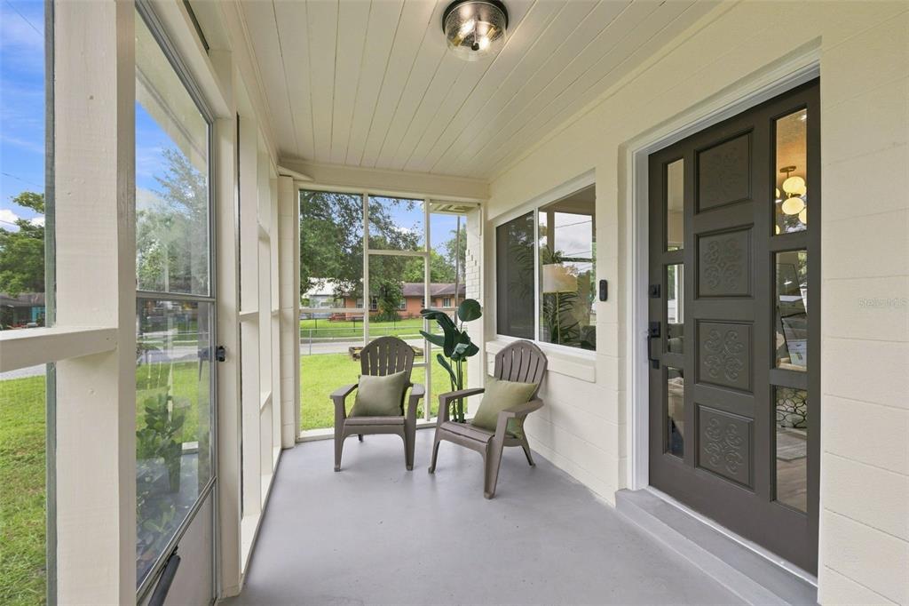 A screened-in porch features a dark brown front door, two chairs, and a light-colored floor — 1825 E HANNA AVENUE, TAMPA, FL