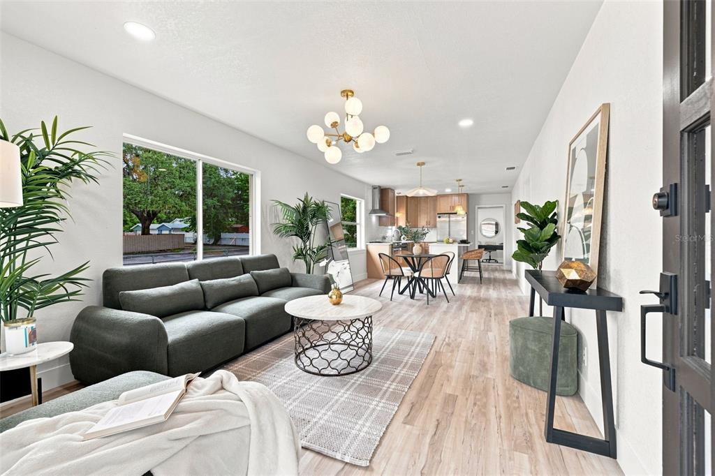 An open-concept living and dining area features light wood flooring, a grey sofa, and modern lighting — 1825 E HANNA AVENUE, TAMPA, FL