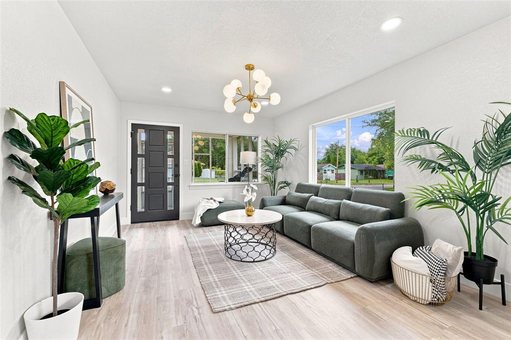 A living room features a grey sofa, a round coffee table, and a modern chandelier — 1825 E HANNA AVENUE, TAMPA, FL