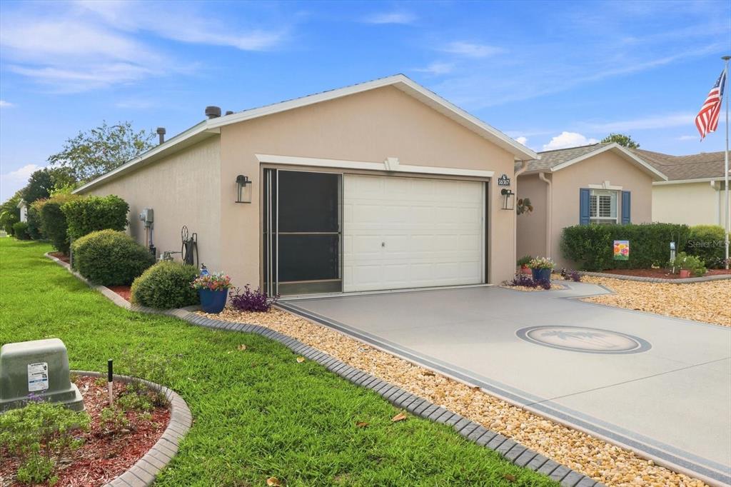 A tan house exterior features a white garage door with a screen and a paved driveway — 16367 SW 13TH TERRACE, OCALA, FL