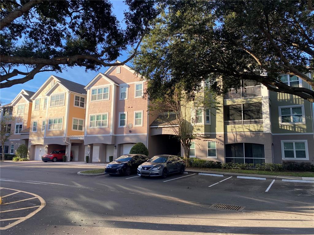 A multi-story apartment building with parking spaces and trees in front — 6685 QUEENS BOROUGH AVENUE UNIT 207, ORLANDO, FL