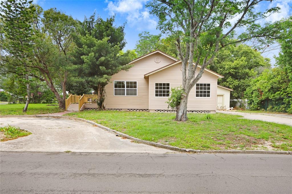 A tan, single-story house with a wooden ramp and a concrete driveway sits among trees — 310 S DELANEY AVENUE, AVON PARK, FL