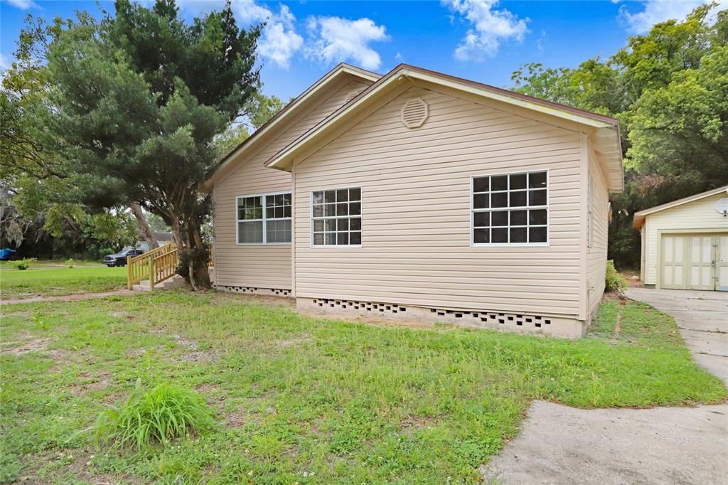 A beige vinyl-sided house with a concrete foundation and a detached garage in the background — 310 S DELANEY AVENUE, AVON PARK, FL