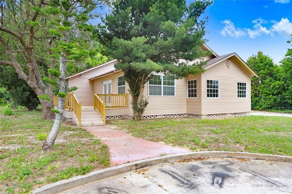 A tan-sided house with a wooden deck and a concrete walkway leading to the entrance — 310 S DELANEY AVENUE, AVON PARK, FL