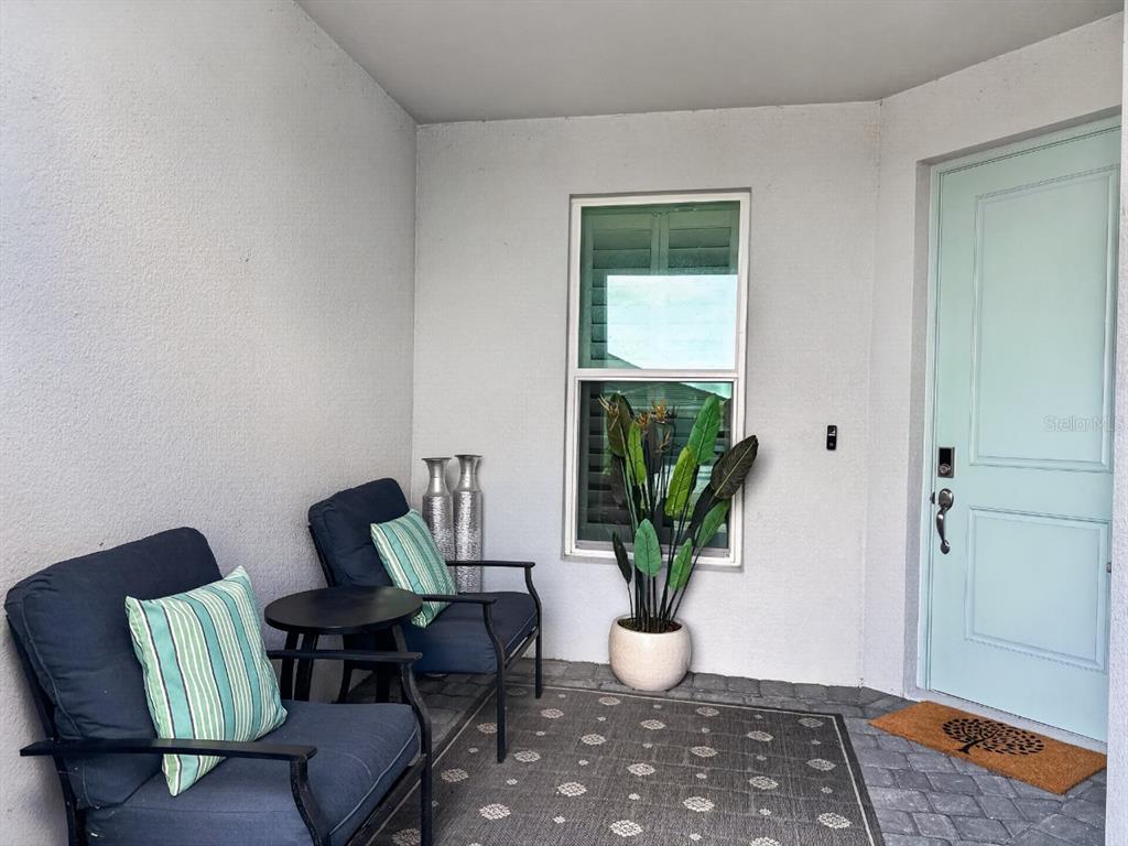 A covered front porch features two dark chairs, a small table, and a potted plant — 8841 OCEANA WAY, NAPLES, FL