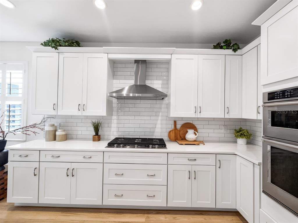 A white kitchen features a gas range, stainless steel vent hood, and subway tile backsplash — 8841 OCEANA WAY, NAPLES, FL
